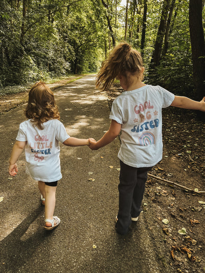 Twee kleine meisjes spelen hand in hand in hun nieuwe, matchende gepersonaliseerde t-shirts van ShirtUp!