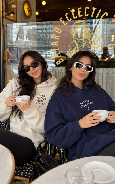 Due amiche indossano felpe personalizzate create con ShirtUp! mentre bevono un caffè insieme.