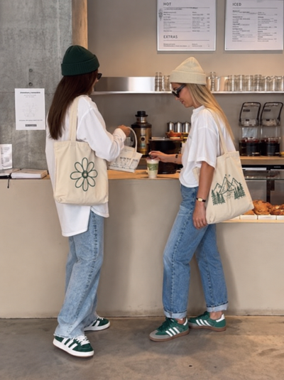 Due donne con tote bag personalizzate create con ShirtUp! mentre prendono un caffè.
